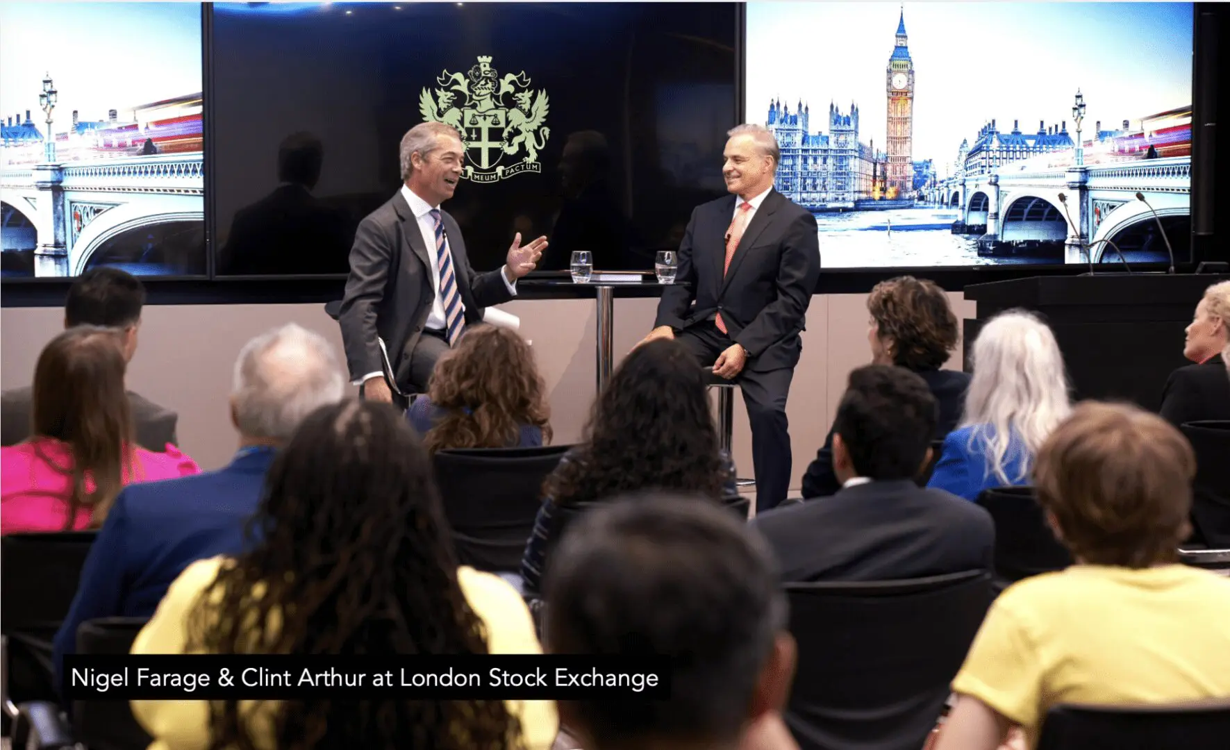 Two men in suit speaking onstage to seated audience